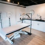 Sala contemporânea de clínica de estética com maca de atendimento, ring light e equipamentos profissionais.