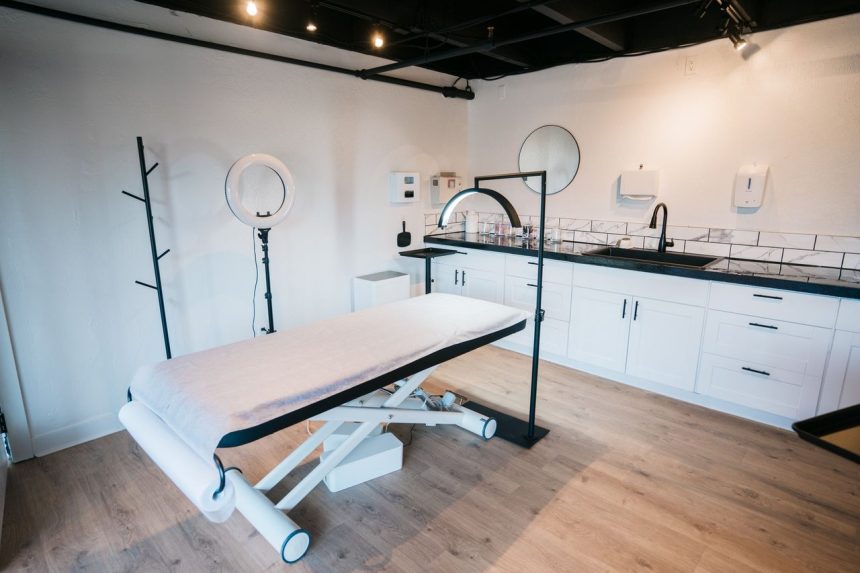 Sala contemporânea de clínica de estética com maca de atendimento, ring light e equipamentos profissionais.