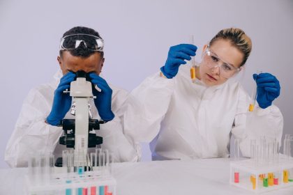 Dois cientistas de jaleco realizam pesquisa em laboratório, usando um microscópio e manipulando tubos de ensaio.